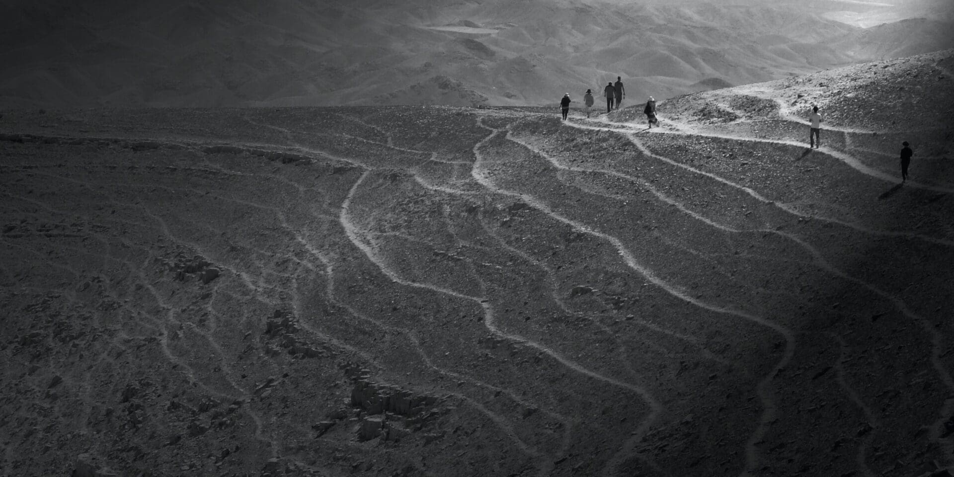 Hikers on winding trails in mountainous landscape.